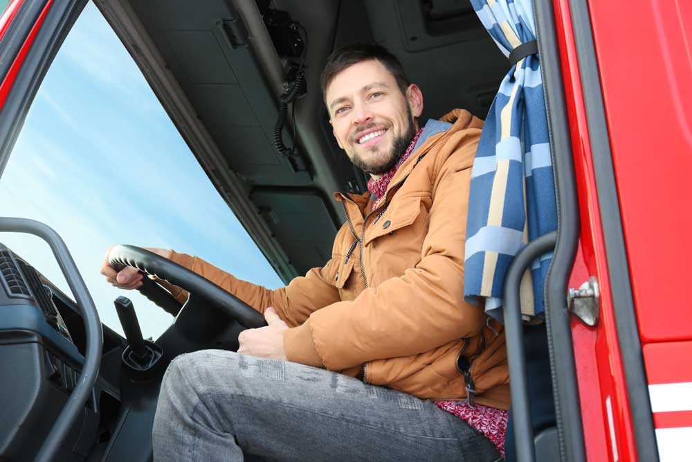 Image of truck driver inside his red truck, smiling.