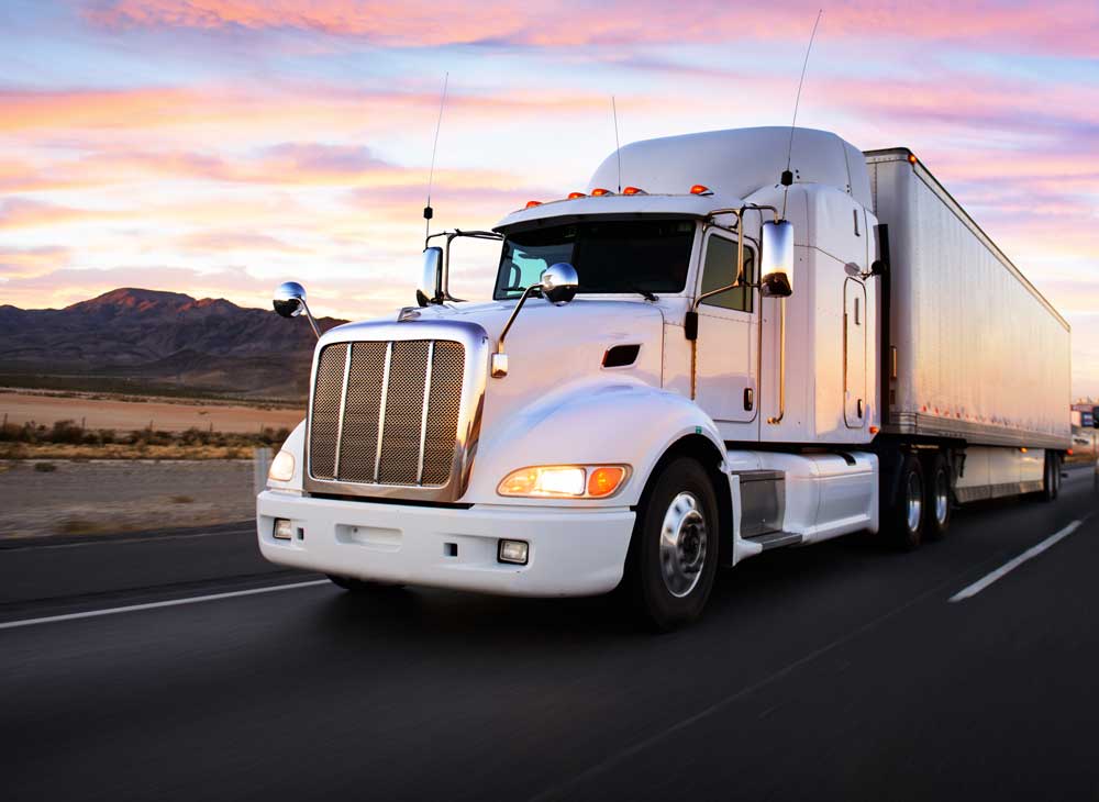 Image of semi-truck driving on the freeway in the sunset.