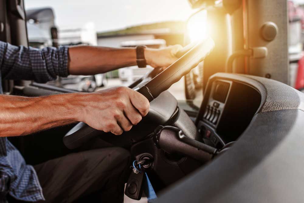 Image of man driving a semi truck while the sun pokes through the image.