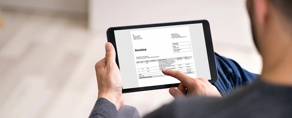 Image of man on a tablet looking at an invoice while he is sitting down. 