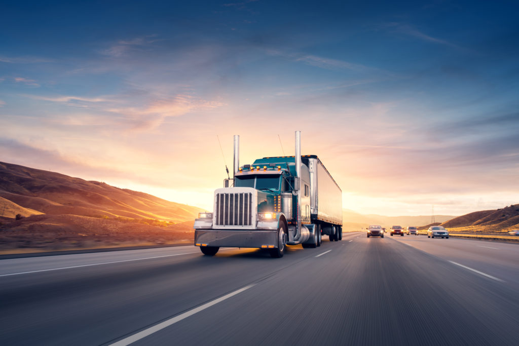 Image of a load carrying truck, driving in the freeway away from the sunset.