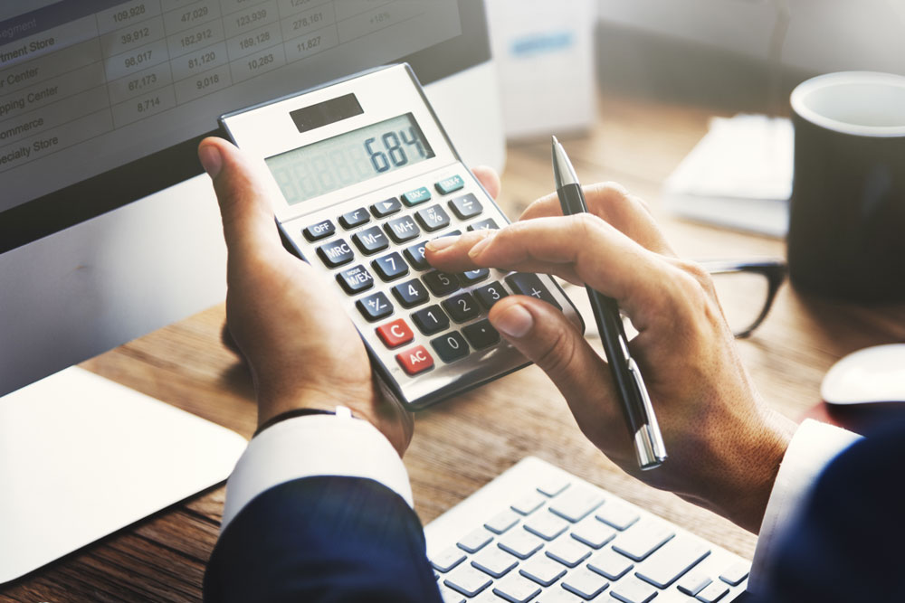 Image of someone using a calculator on their desk in front of their computer.