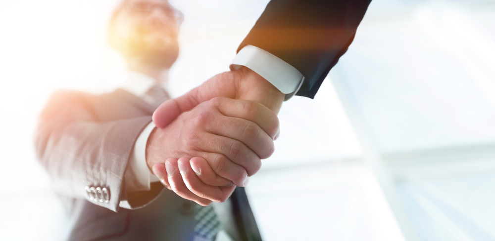 Image of two business people smiling and shaking each other's hand. 