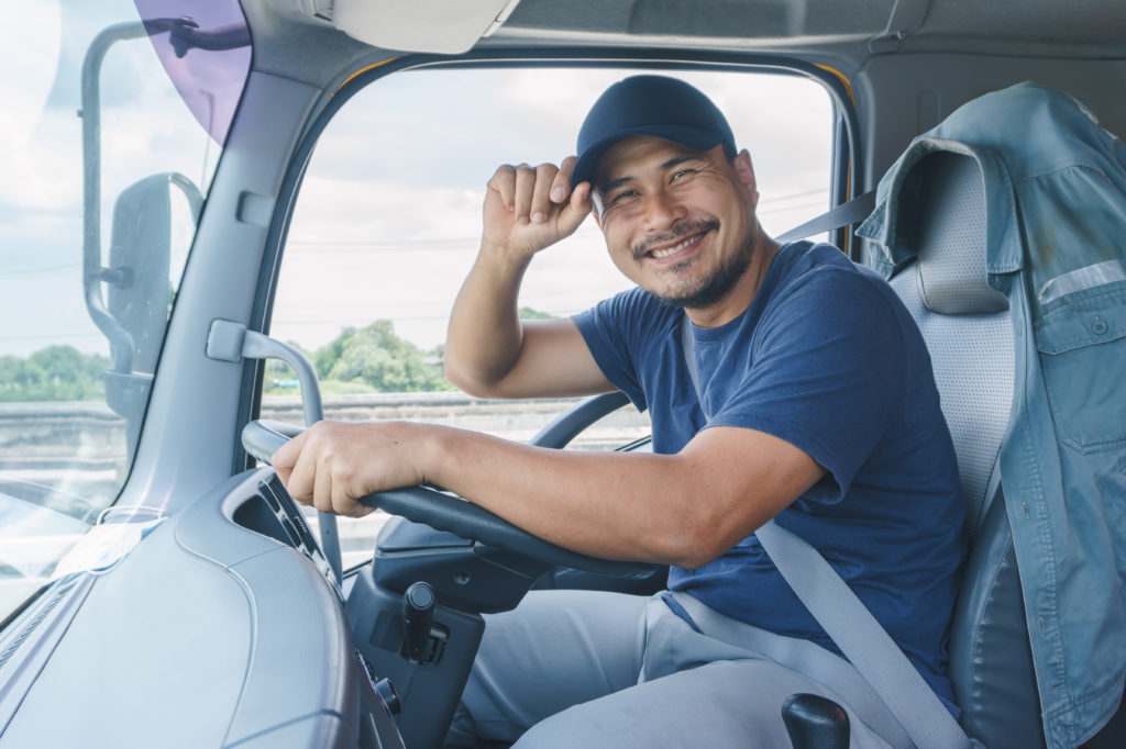 Image of semi truck driver smiling and tipping his hat. 