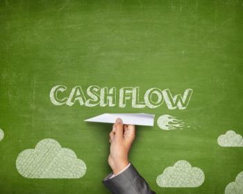 Image of a chalkboard drawing with the word cash flow written on it. Someone holds a paper plane against the chalkboard drawing.