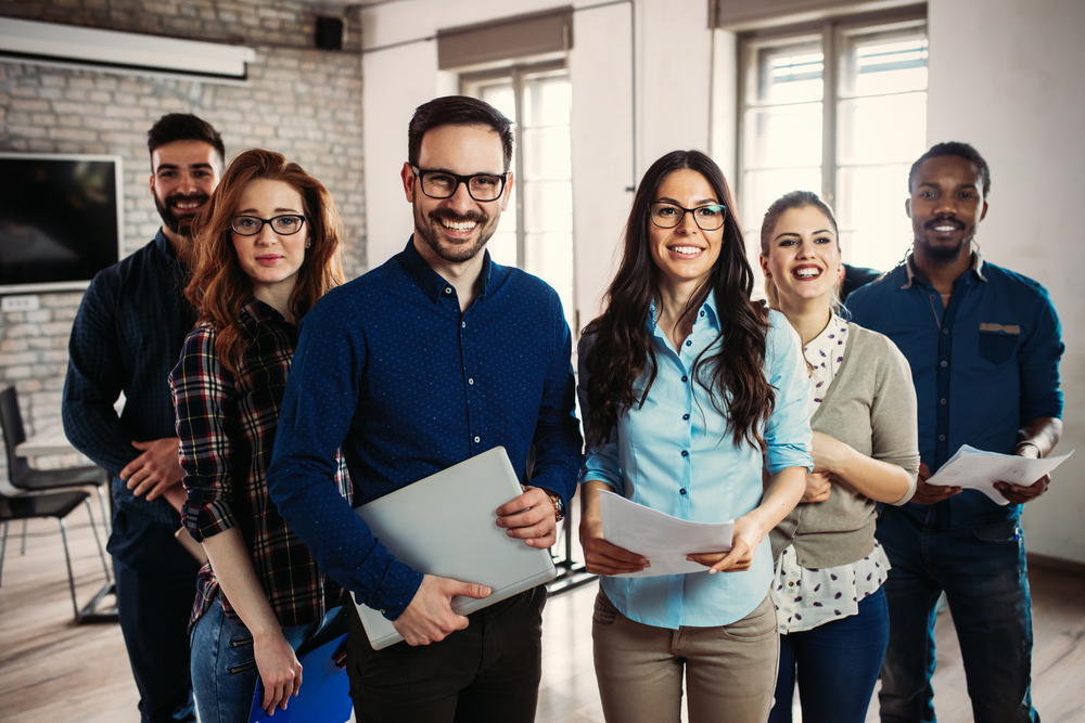 Image of a group of coworkers side by side smiling in their office.