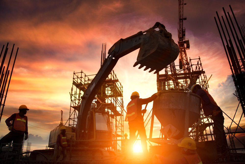 Sunset image of a construction site with an excavator and construction workers actively working.