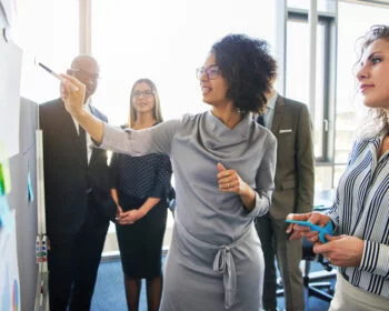 Businesswoman presenting ideas on a whiteboard to her colleagues during a meeting.