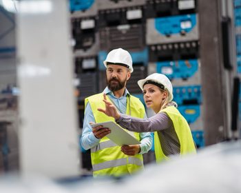 Warehouse workers in safety vests reviewing operations on a tablet in a distribution facility